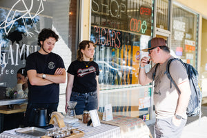 Two baristas and a customer tasting coffee in front of coffee shop