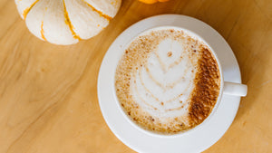 Chai latee on a white saucer on a wood table with a hint of pumpkins